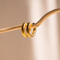 Two Chunky Hoops dangle from a curved beige rod against a soft, neutral background—an elegant display that highlights the bold style of these classic earrings.