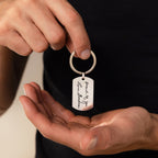 Someone holds a Handwriting Dog Tag Keychain personalized with "proud of you, Love, Grandma" engraved on it.