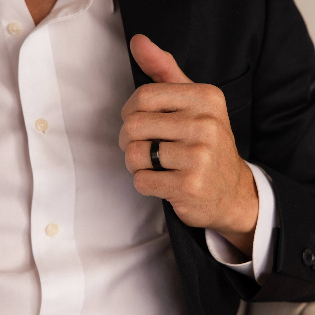 A person in a suit adjusts their jacket, showcasing a minimalist ring from the Classic Men's Black Rings Set on their left hand.