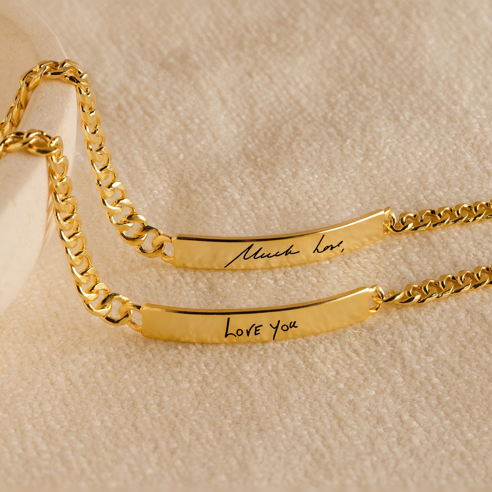 A pair of Men's Engraved Bar Bracelets, featuring Much love and Love you messages, displayed on beige fabric. This personalized bracelet set is a meaningful memorial gift or keepsake.