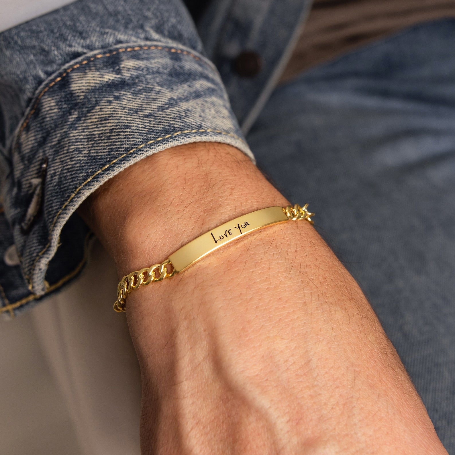 A Men's Engraved Bar Bracelet inscribed with “Love you” peeks out from under a denim jacket sleeve—perfect as a personalized or memorial gift.