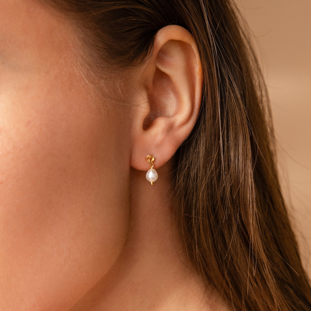 Close-up of a woman's ear showcasing the Knot Pearl Necklace & Earrings Set, featuring elegant gold accents and a white pearl drop—an ideal gift for her.