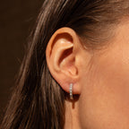 Close-up side view of a silver pearl huggie earring worn by a model with straight hair.