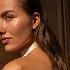 Model wearing gold pearl huggie earrings with natural makeup and sunlight highlighting her skin.