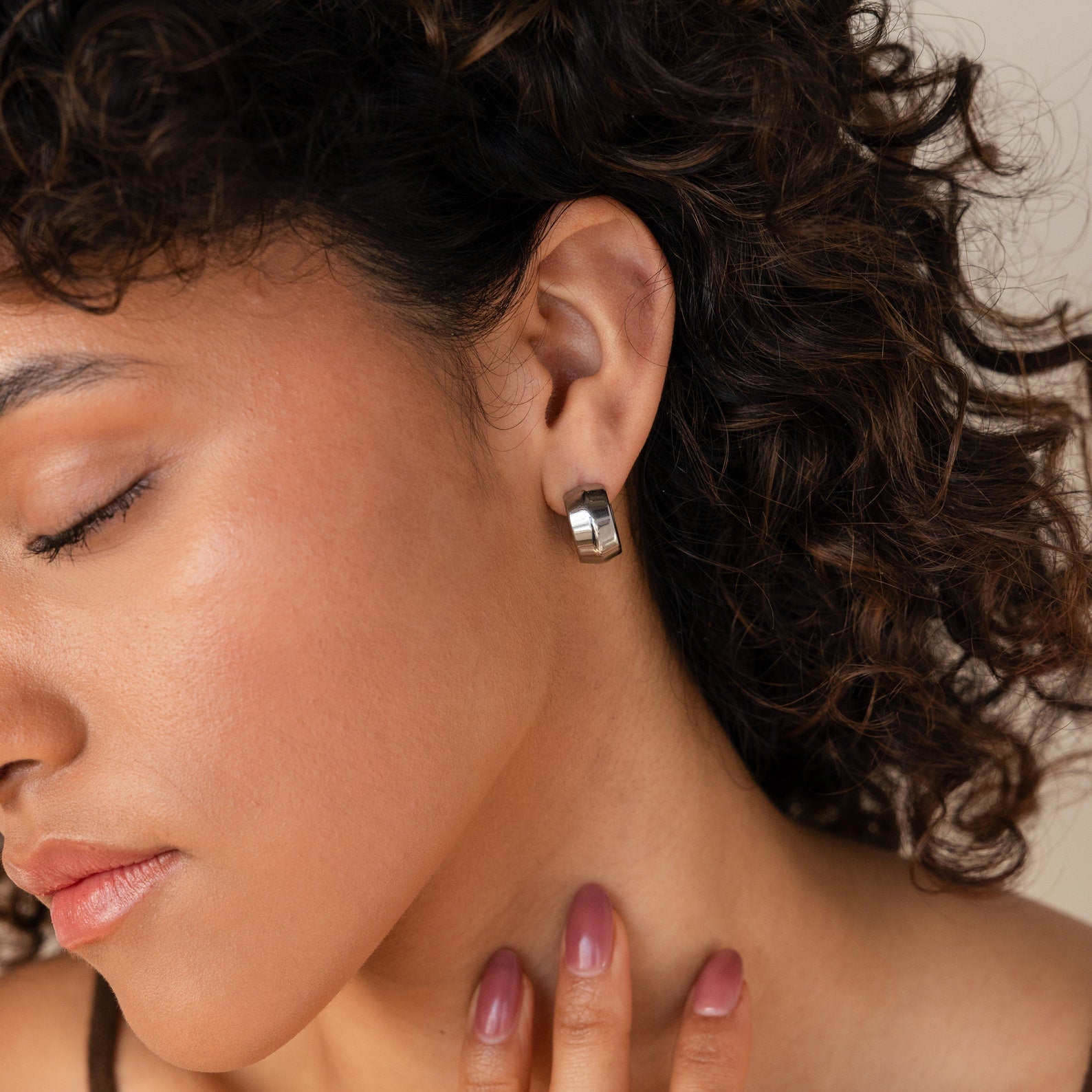 With her eyes closed and hand on her neck, a woman with curly hair wears Chunky Bold Hoops—trendy earrings that make a statement in any look.