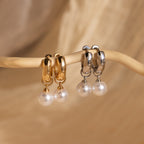 The Bold Pearl Drop Earrings feature gold and silver hoops with pearl dangles, making a striking statement and beautifully displayed on a curved beige branch.