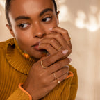 Woman in a mustard sweater displays her Pearl Diamond Stacking Rings on her fingers, gazing thoughtfully to the side.