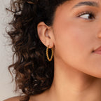 Close-up of a woman with curly hair wearing Bold Twisted Hoops in her left ear, highlighting their unique twist design.