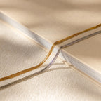 Close-up of a beige book with gold and silver ribbon bookmarks on a textured cream surface, beside a delicate Multi Strand Chain Necklace.