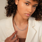 A woman in a cream blazer gently touches a strand of her Multi Strand Chain Necklace, the minimalist silver jewelry catching the light as she looks at the camera.
