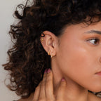 A woman with curly hair, pink nails, and multiple gold earrings highlights her ear adorned with Dainty Opal Earrings.