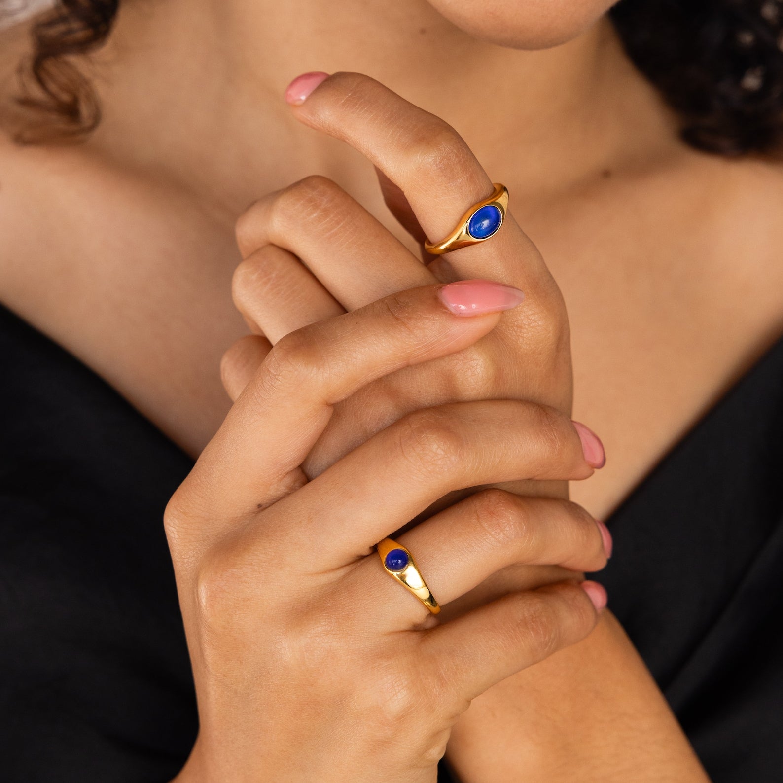 A woman with pink nails wears the Signet Mood Rings Set, featuring blue stones, as she crosses her hands near her face.