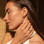 Close-up of a model wearing gold pearl huggies, touching her neck with manicured fingers and wearing gold rings.