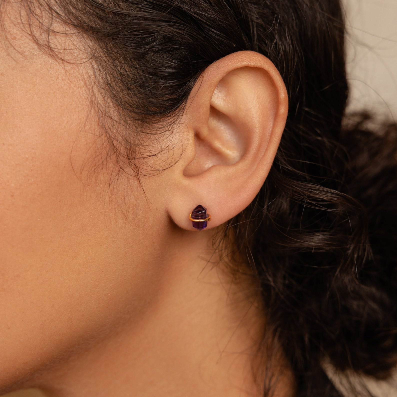 Close-up of a woman's ear wearing Amethyst Herkimer Studs—enchanting small purple gemstones wrapped in gold wire.