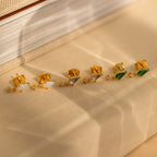 Three pairs of Art Deco Drop Studs—featuring opal, CZ diamond, and green stones—are displayed on a beige textured surface.