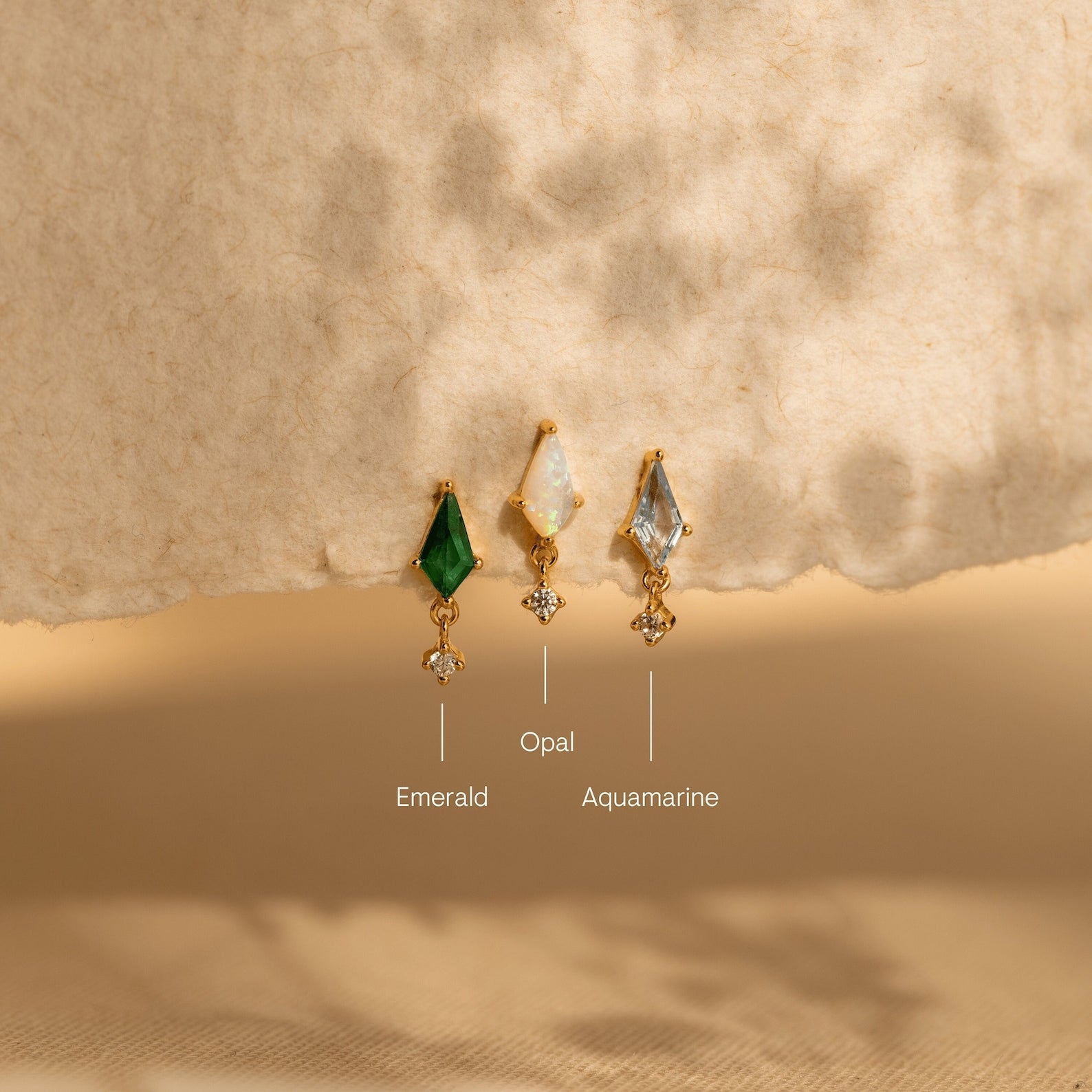 A row of gemstone earrings in various shapes and colors, including Art Deco Drop Studs, CZ Diamond, and Kite Gemstone Studs.