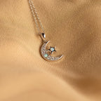 The Opal Moon & Star Necklace showcases a gold crescent moon and star pendant with opal details, elegantly displayed on a soft beige fabric background.