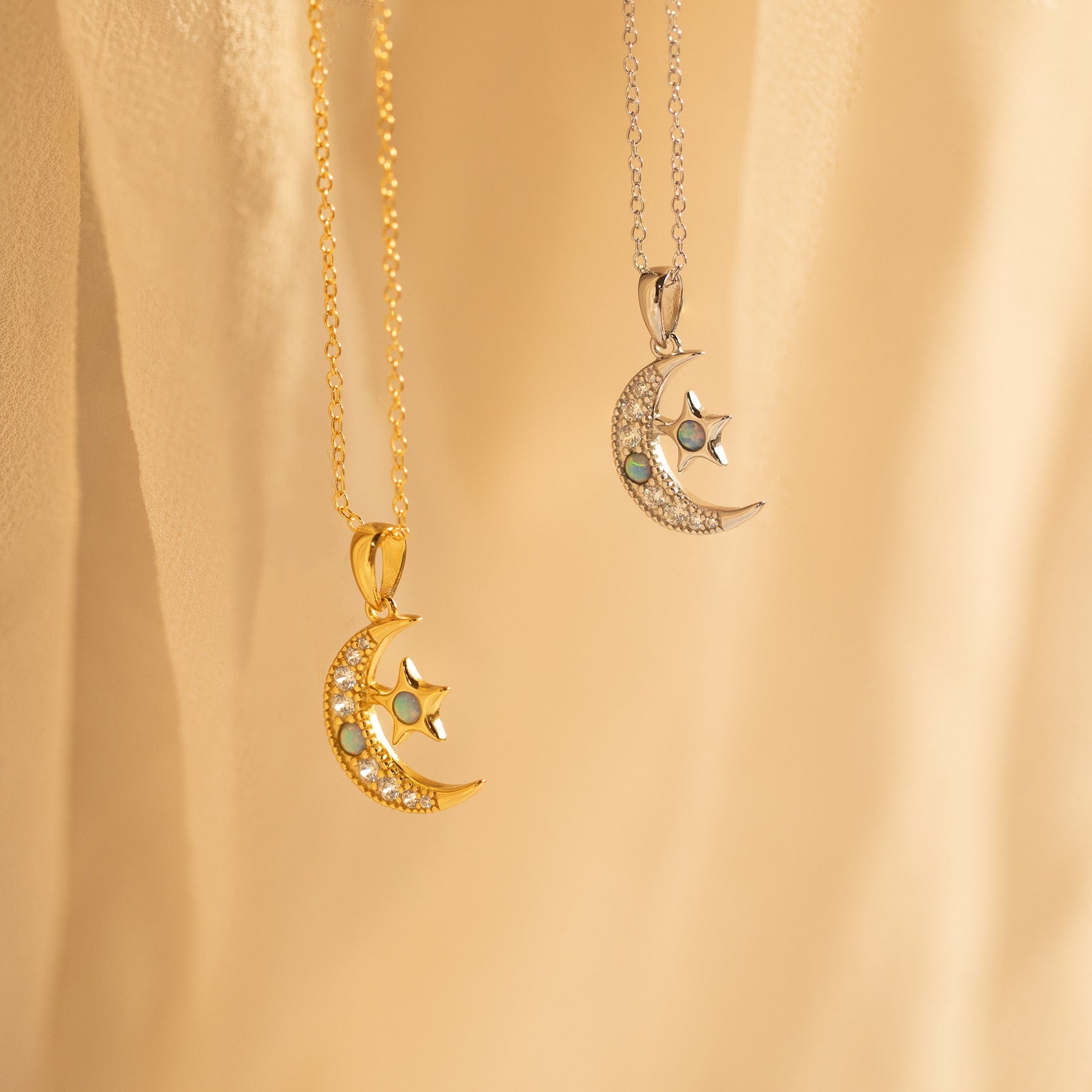 Two crescent moon and star necklaces—one gold, one silver—hang against a soft beige background, making a celestial duo perfect for layering with your favorite Opal Moon & Star Necklace.