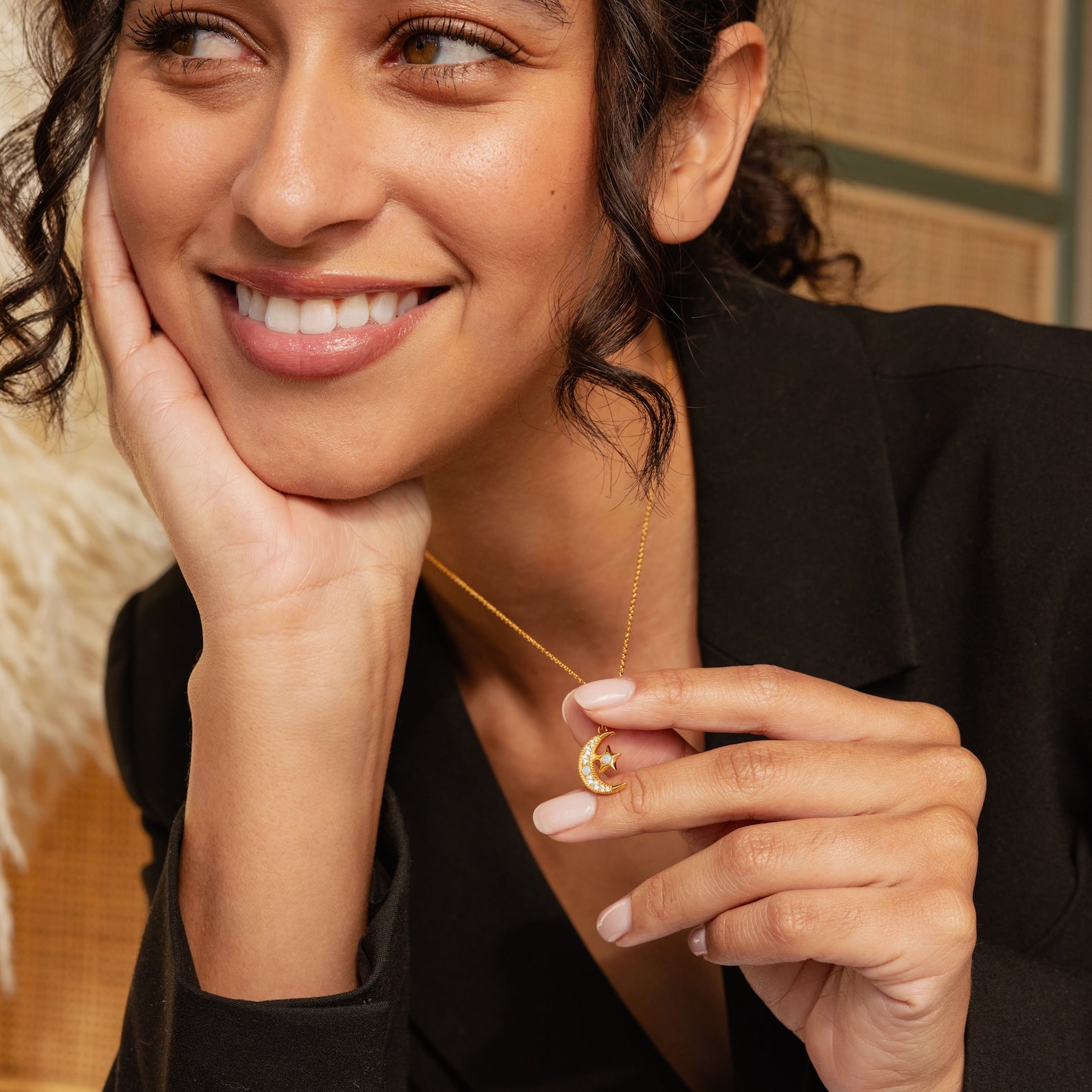Smiling woman in a black blazer holding the Opal Moon & Star Necklace, featuring a celestial-themed pendant with shimmering details.