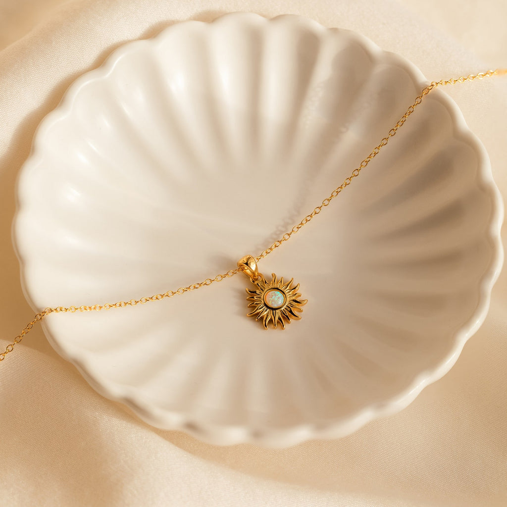 Opal Sun Necklace: This dainty gold necklace features a sun-shaped design with a central white opal, beautifully presented in a scalloped cream dish—an ideal jewelry gift.