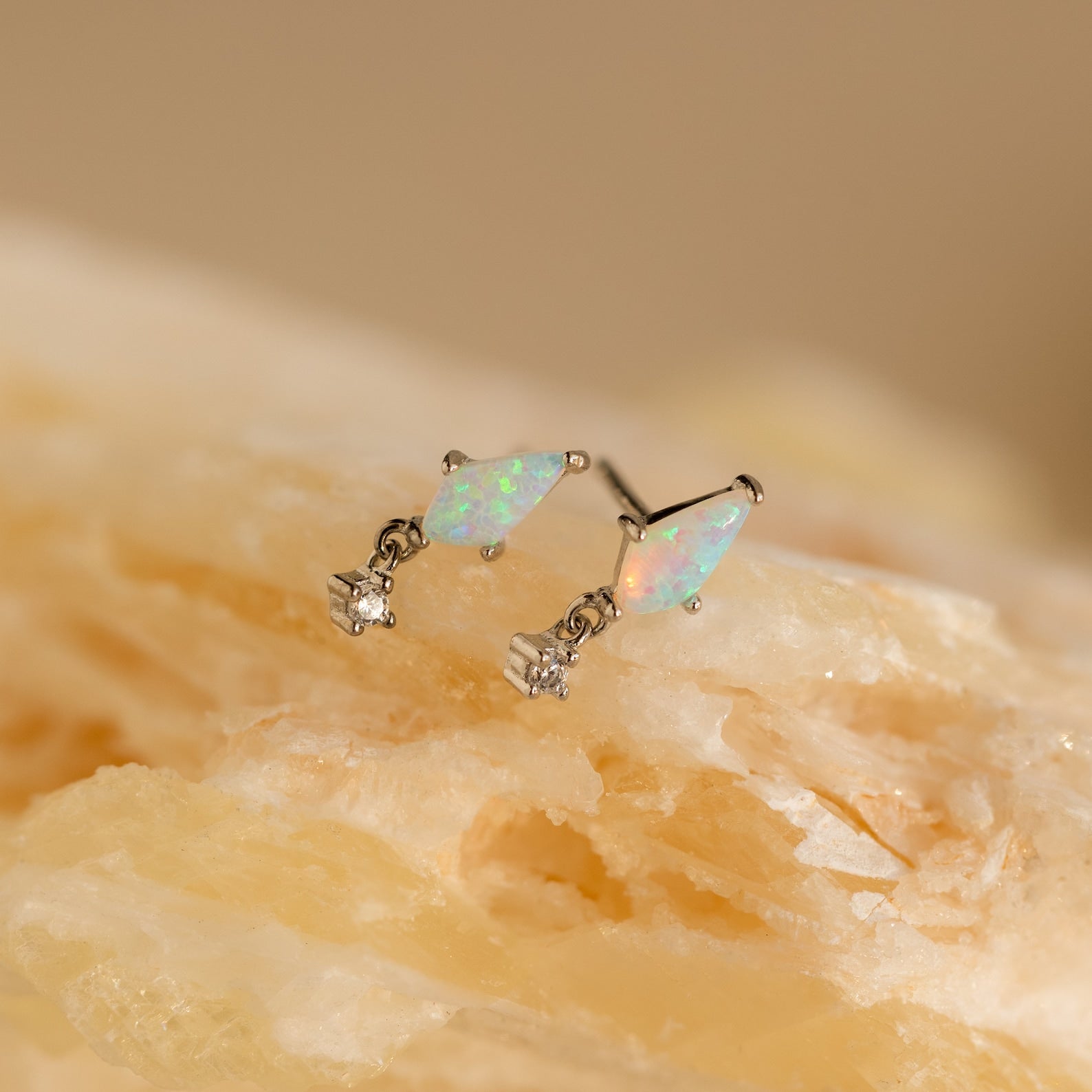 The Opal Kite Drop Earrings, featuring a striking geometric design, rest elegantly on a rock.