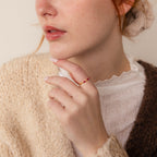 Woman wearing a textured sweater and the Triple Marquise Birthstone Ring, featuring delicate stacking with small red beads, hand near her face.