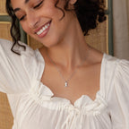 Smiling woman in a white blouse wearing a silver western style necklace featuring a small cowboy boot pendant.