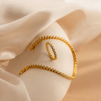 The Diamond Bezel Tennis Ring, paired with a gold bracelet and necklace featuring round gems, is displayed on soft beige fabric under gentle lighting.