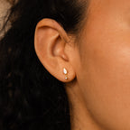 Close-up of a person's ear adorned with Art Deco Drop Studs featuring gold and white stones, with curly dark hair visible.
