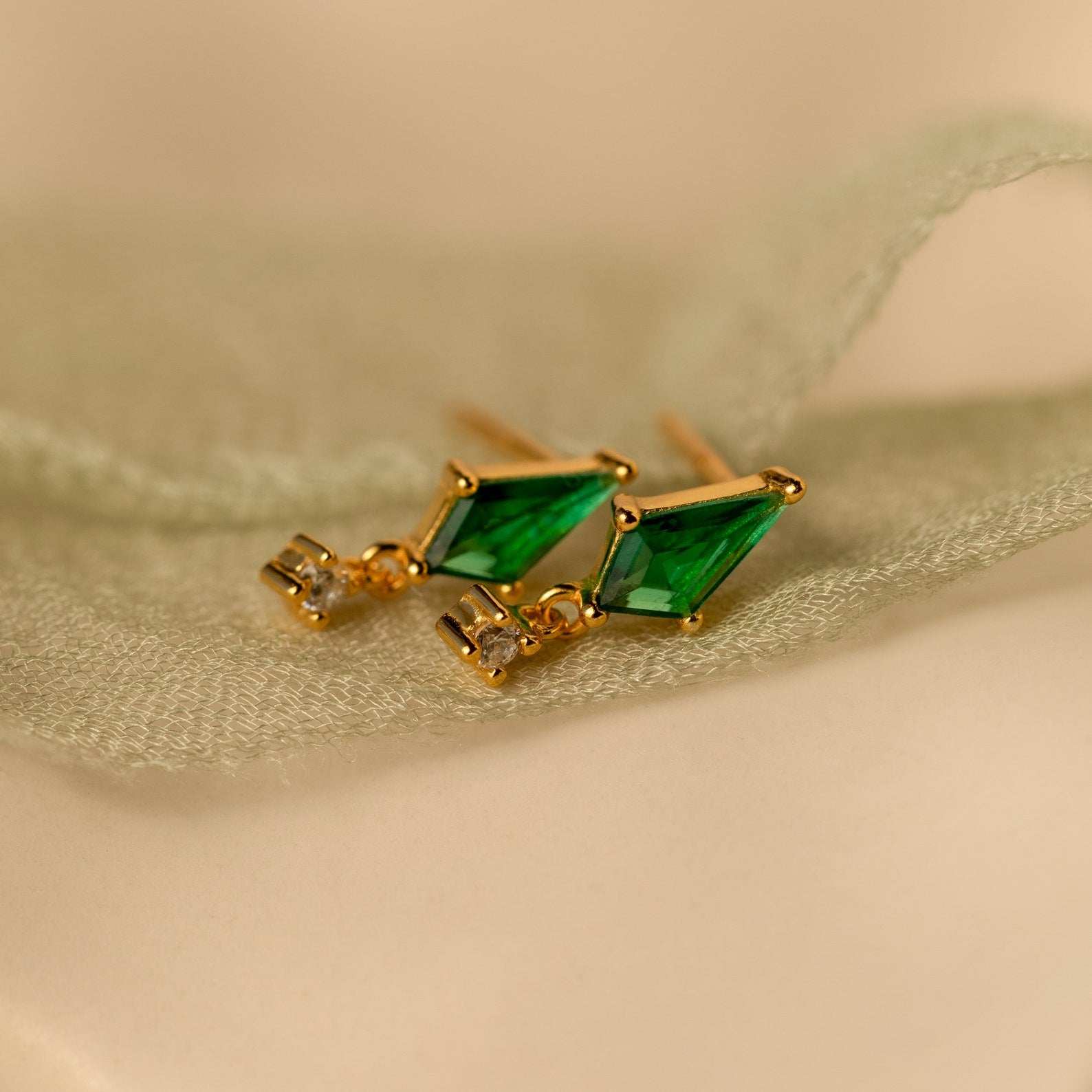 Art Deco Drop Studs feature green gemstone triangles and sparkling CZ diamonds, elegantly displayed on light green fabric.