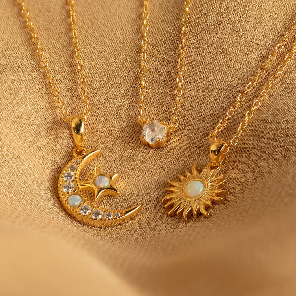 The Opal Moon & Star Necklace shines beautifully on soft beige fabric, highlighting its gold finish and celestial charms.