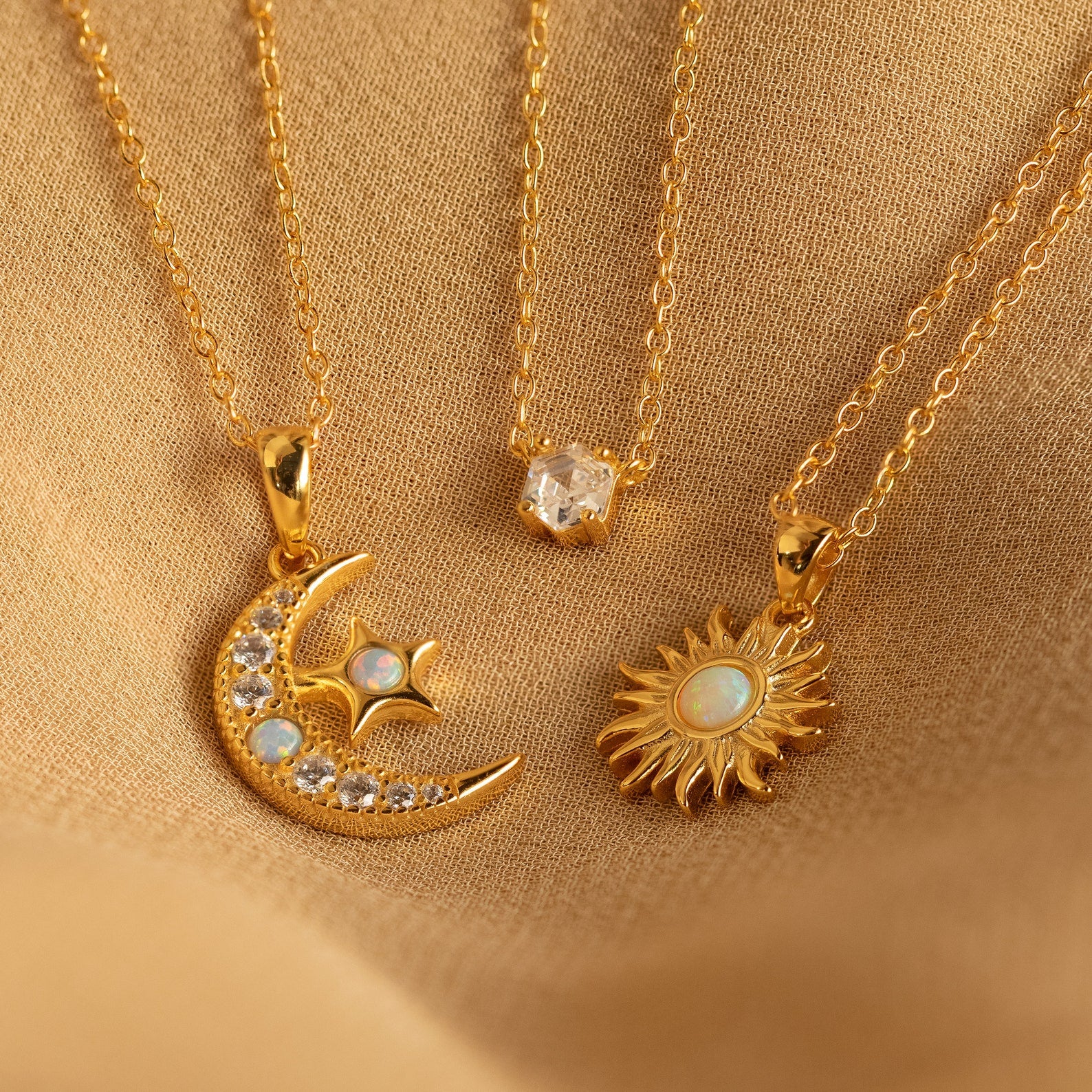 The Opal Moon & Star Necklace shines beautifully on soft beige fabric, highlighting its gold finish and celestial charms.