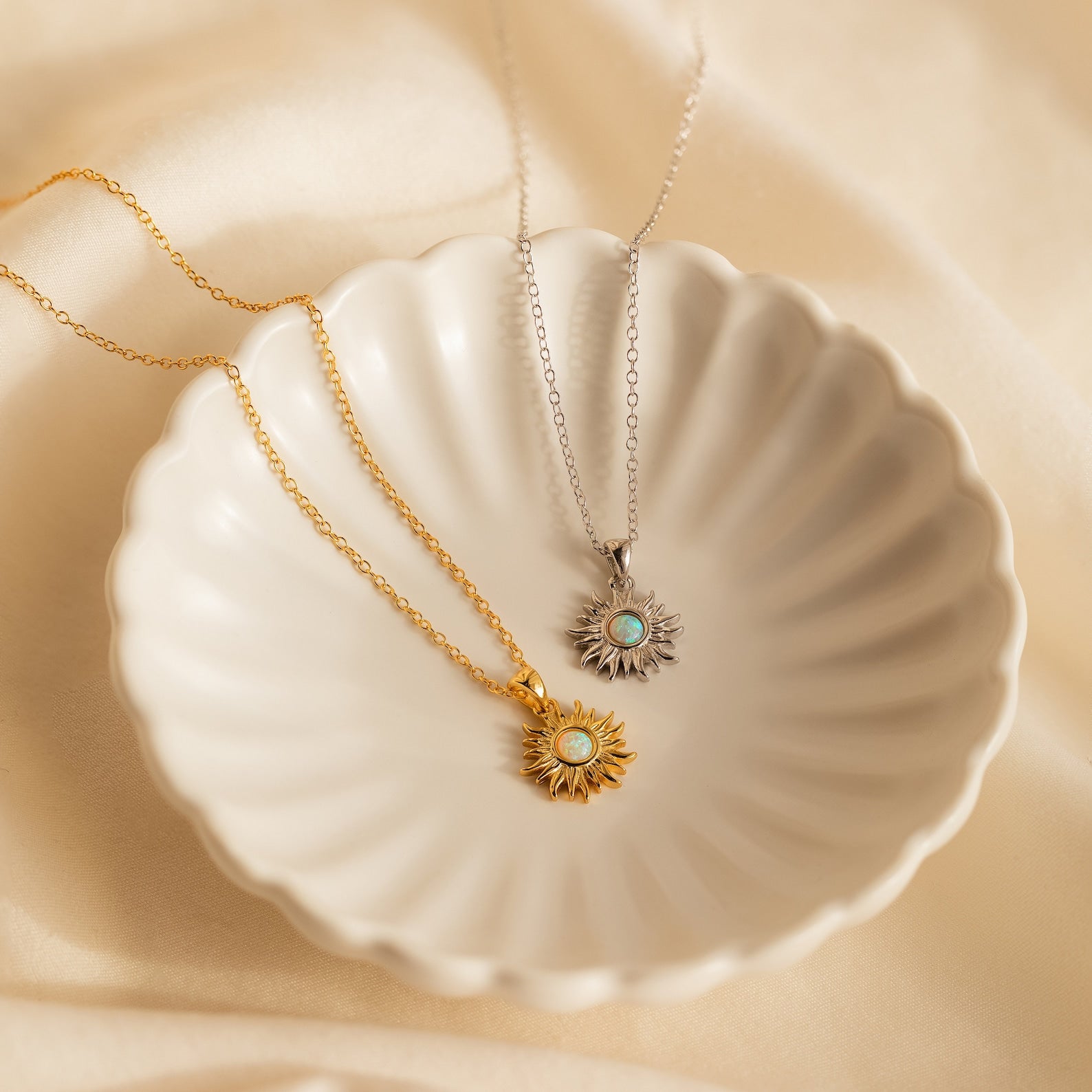 The Celestial Pendant Necklace Set in gold and silver, each with a turquoise center, is displayed on a white scalloped dish atop cream fabric—a perfect gift for her.