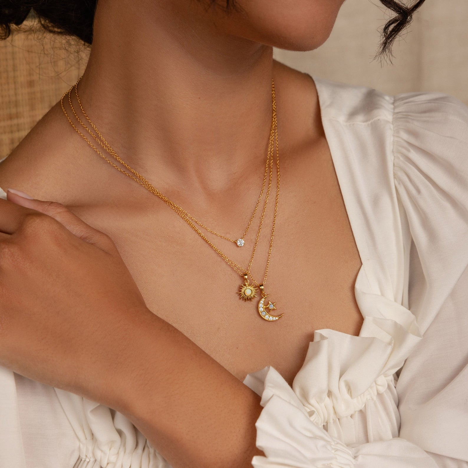 Woman wearing layered gold necklaces, including the Opal Sun Necklace with sun, moon, and star pendants over a white blouse—a dainty, thoughtful jewelry gift.
