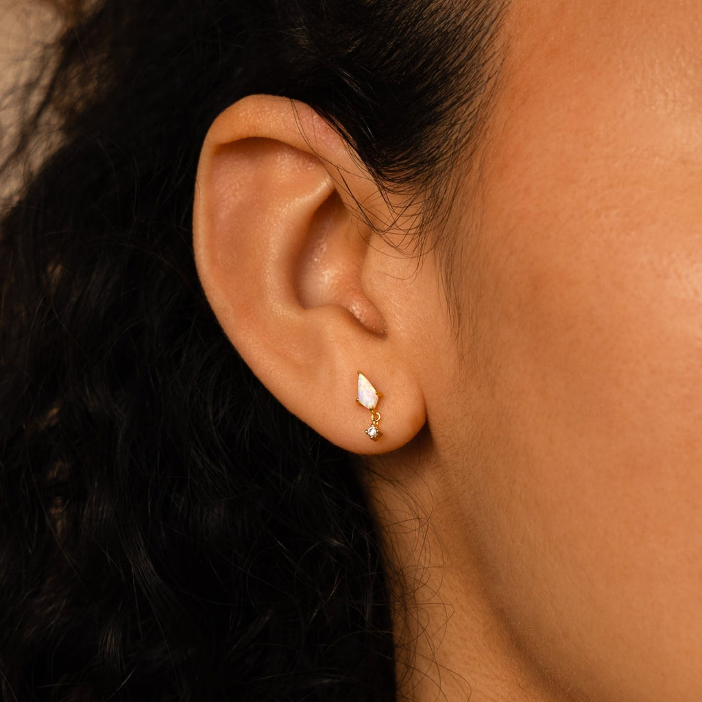 Close-up of a woman's ear wearing Opal Kite Drop Earrings—one teardrop-shaped, one round, with subtle geometric designs. The earrings feature an elegant CZ Diamond accent for extra sparkle.