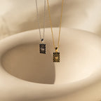 The Celestial Pendant Necklace Set features two rectangular sunburst pendants in silver and gold on a beige ceramic background, accented with opal and diamonds—an ideal gift for her.
