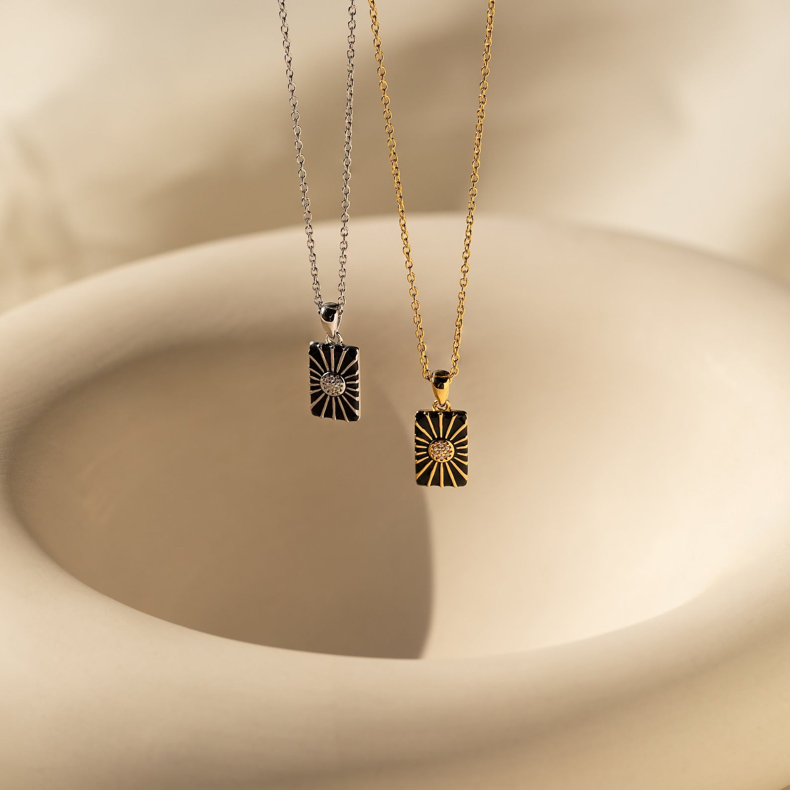 The Celestial Pendant Necklace Set features two rectangular sunburst pendants in silver and gold on a beige ceramic background, accented with opal and diamonds—an ideal gift for her.