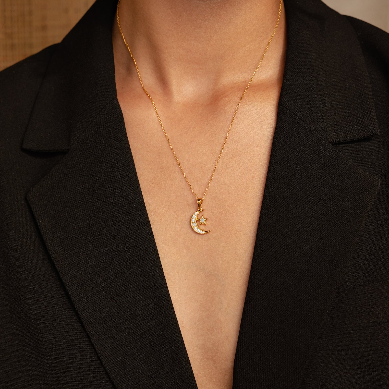 A person wearing a black blazer and the Celestial Pendant Necklace Set, featuring a gold crescent moon and star pendant—an elegant gift for her.