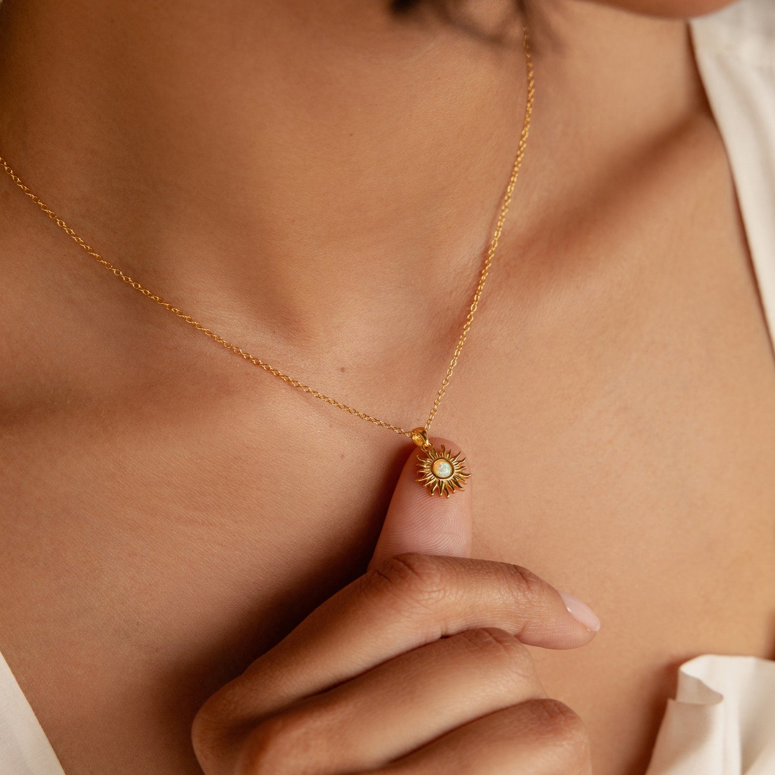 A person holds the Celestial Pendant Necklace Set featuring a gold sunburst design with a white opal and diamond center on their chest—the perfect gift for her.