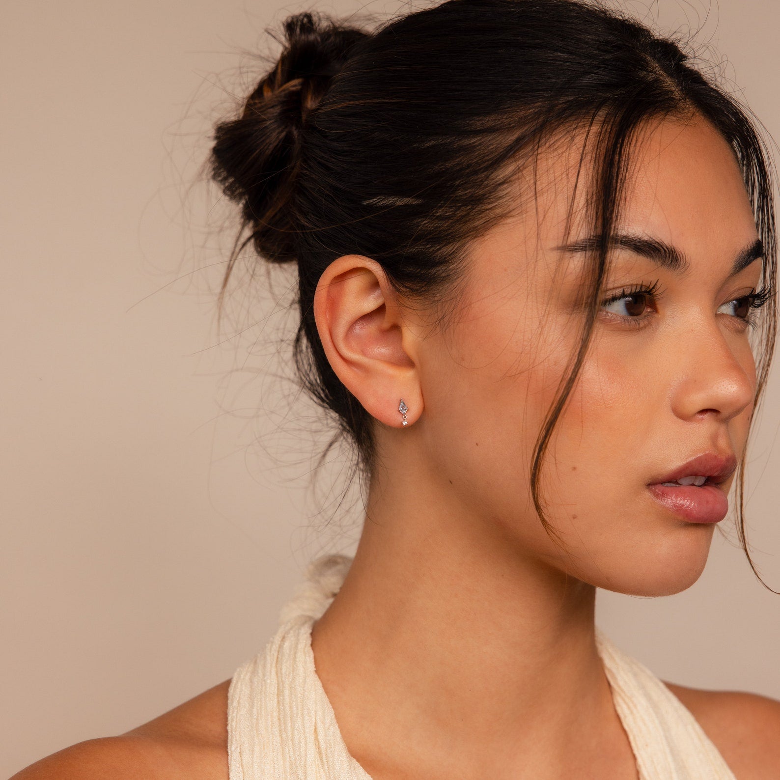 Woman with dark hair in a bun, wearing a cream halter top and elegant Aquamarine Kite Drop Earrings, looking to the right.