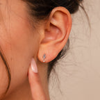 Close-up of a woman's ear adorned with Aquamarine Kite Drop Earrings; her finger gently touches her earlobe, highlighting the earrings' elegant design and sparkling aquamarine stones.