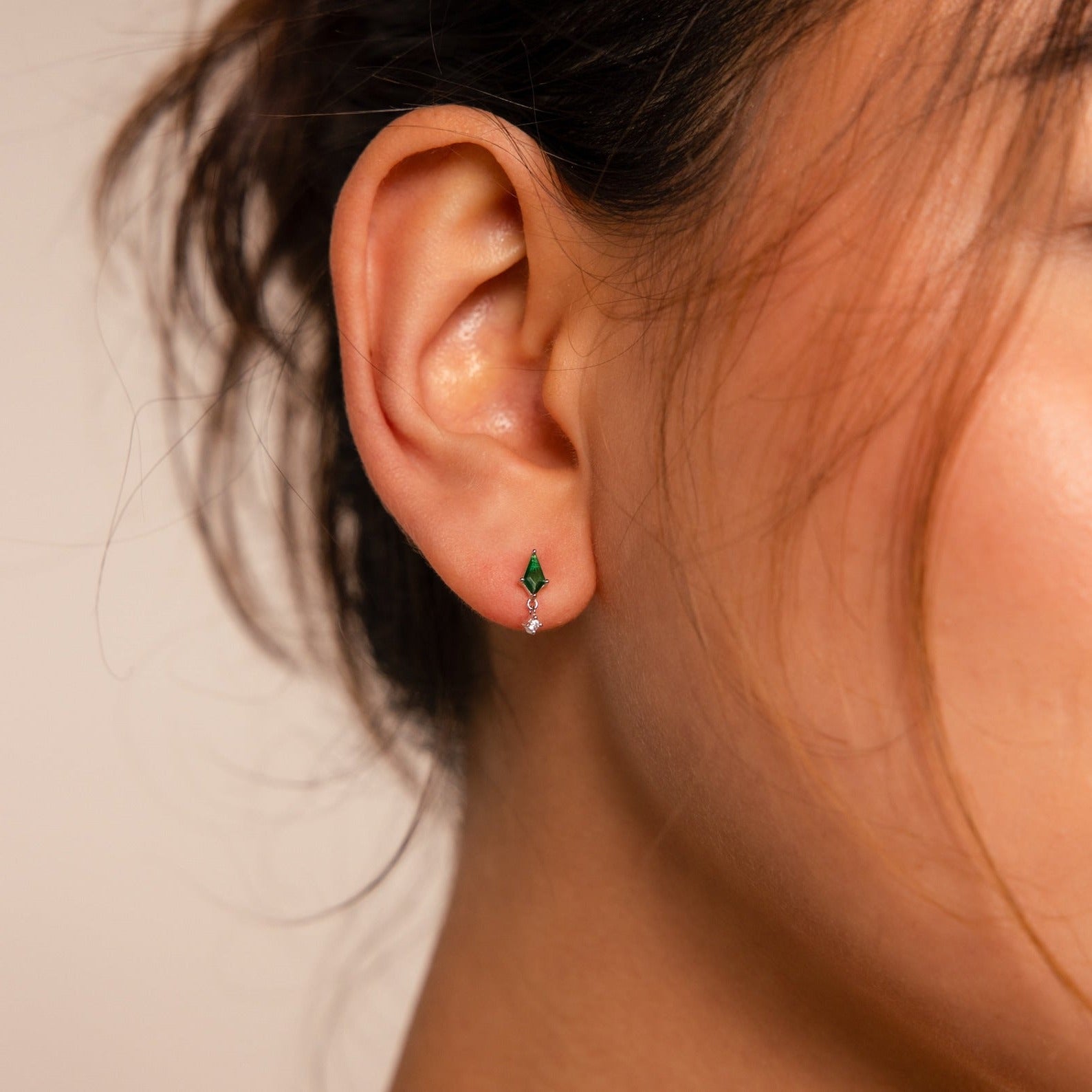 Close-up of a person's ear wearing Emerald Kite Drop Earrings, featuring a stylish green and white decorative design.