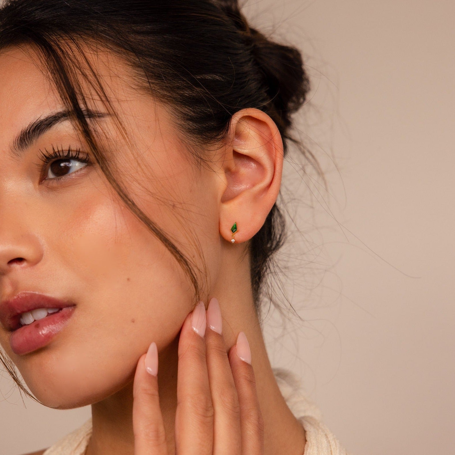 A woman with her hand on her cheek showcases elegant Emerald Kite Drop Earrings, adding a touch of sophistication to her look.