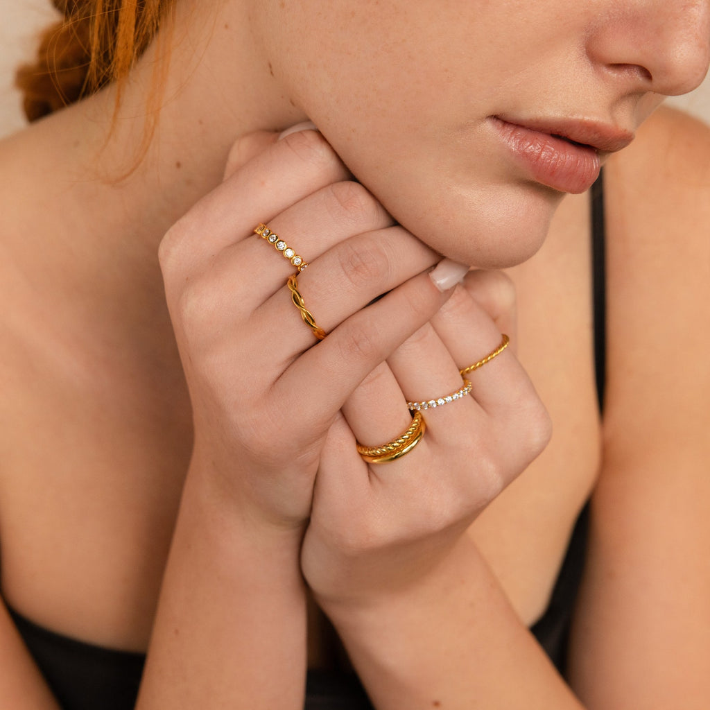 A fair-skinned woman in a black top wears a Diamond Bezel Tennis Ring adorned with CZ diamond gemstones, holding her hands to her chin.