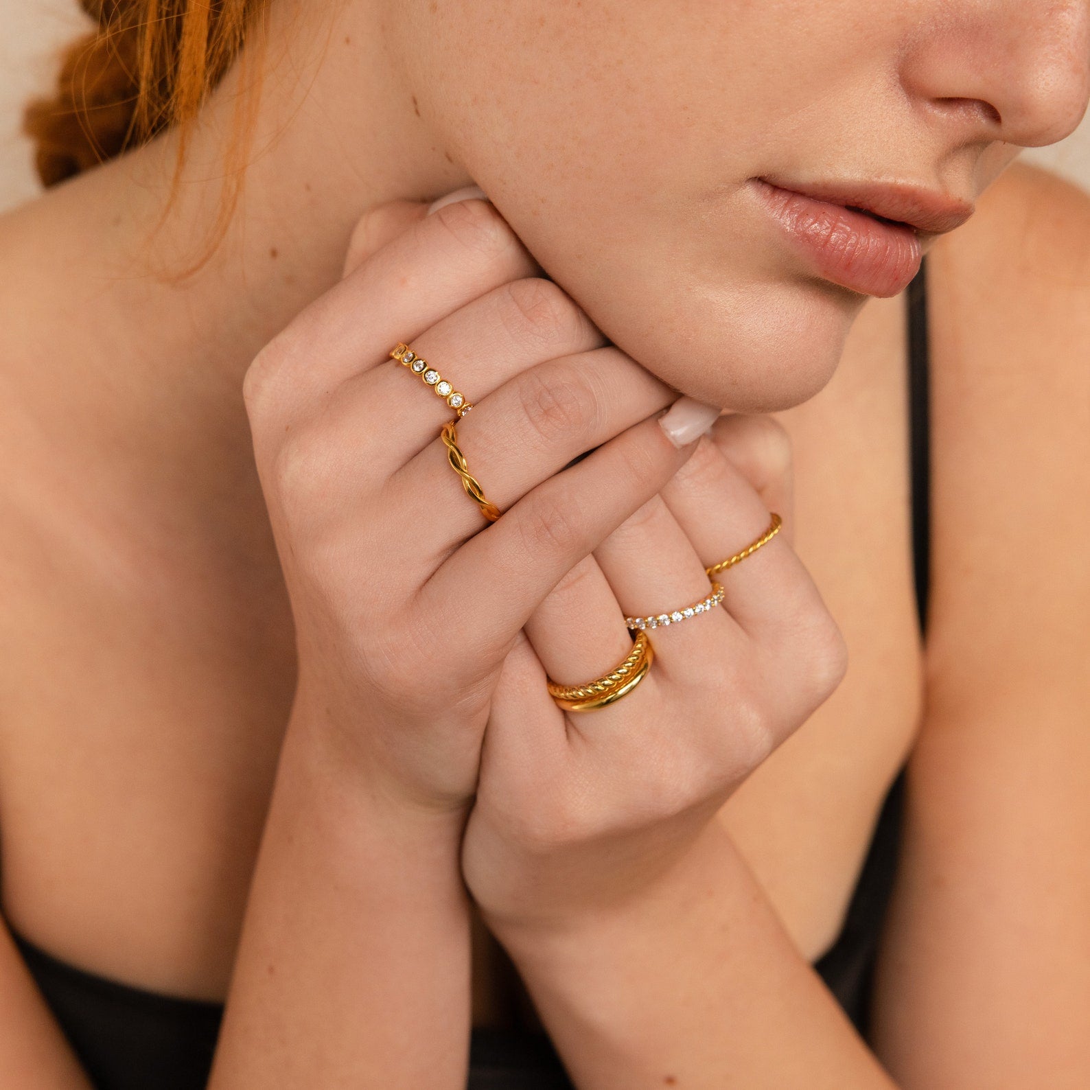 A fair-skinned woman in a black top wears a Diamond Bezel Tennis Ring adorned with CZ diamond gemstones, holding her hands to her chin.