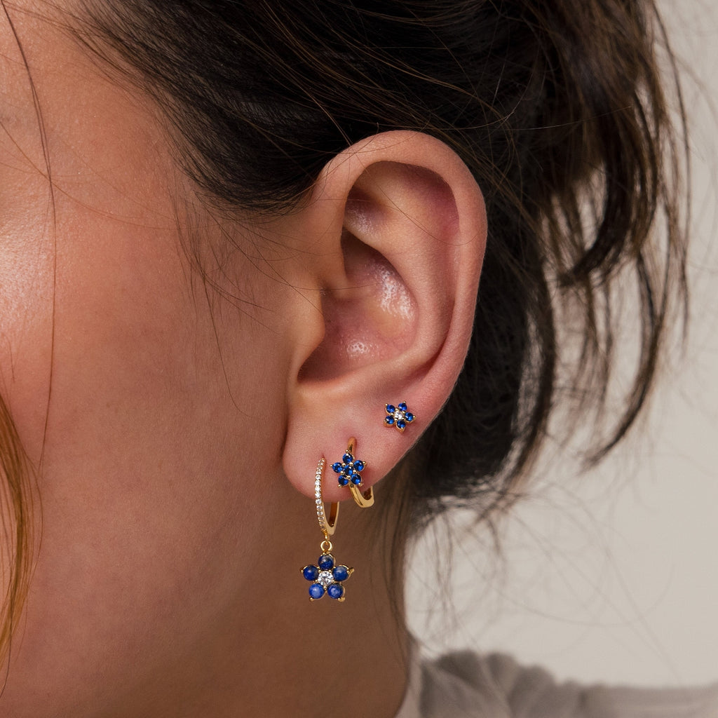 Close-up of a woman's ear adorned with the Sapphire Flower Earrings Set, featuring three gold earrings with blue sapphire flower designs—an elegant option for lovers of unique gemstone jewelry.