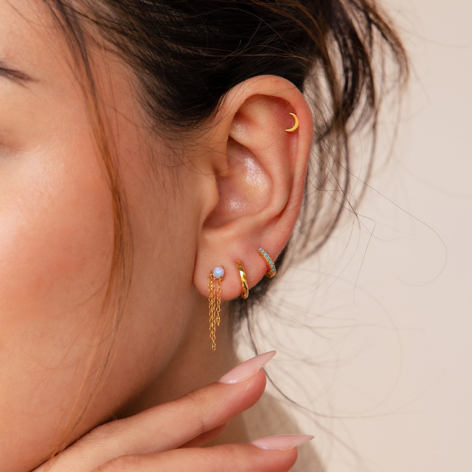 Close-up of a woman's ear adorned with Opal Chain Earrings, featuring gold hoops, a crescent, an opal stud, and chain dangles—perfect for elevating any jewelry collection.