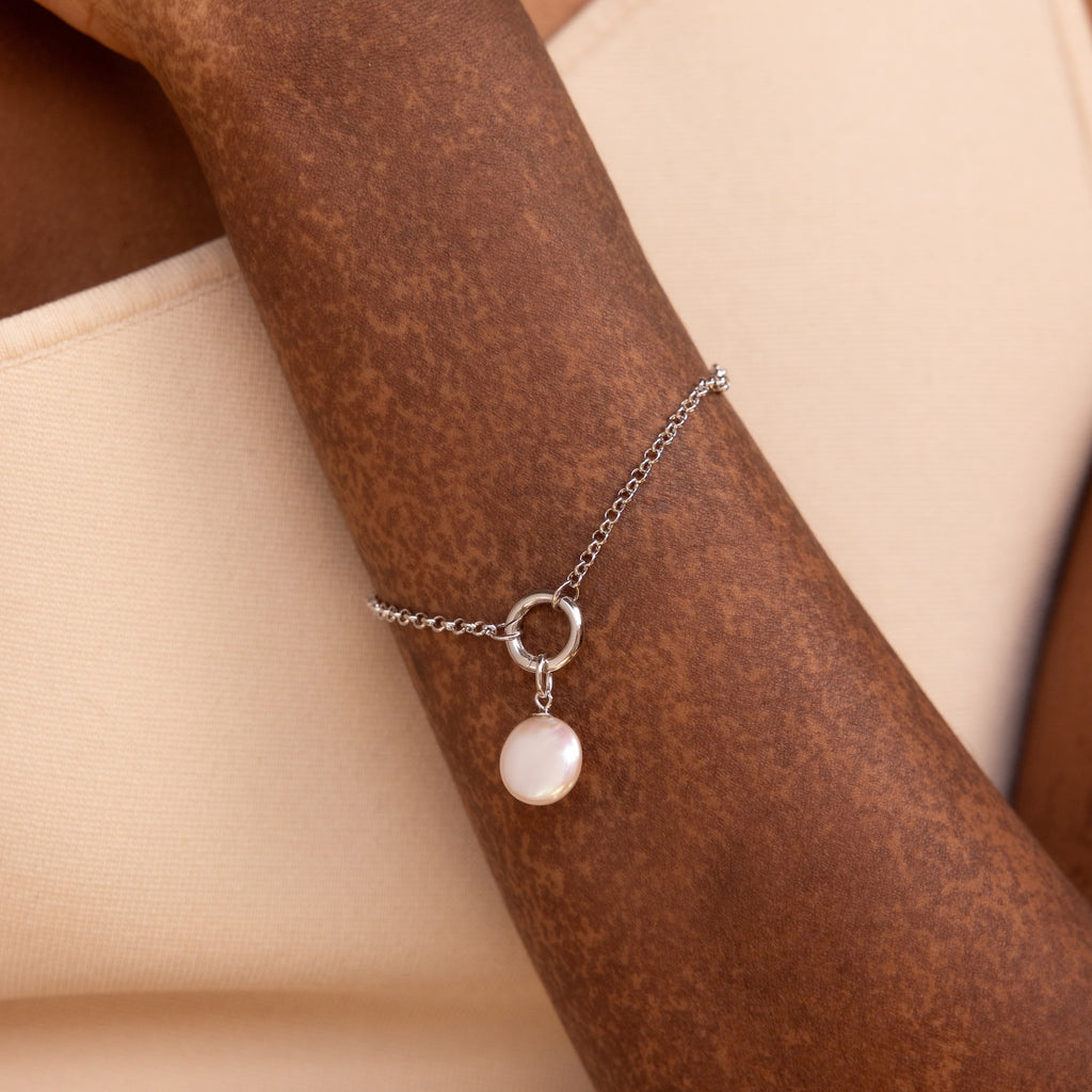A person wears the Round Pearl Charm in Sterling Silver on their wrist, perfectly paired with a cream-colored top.
