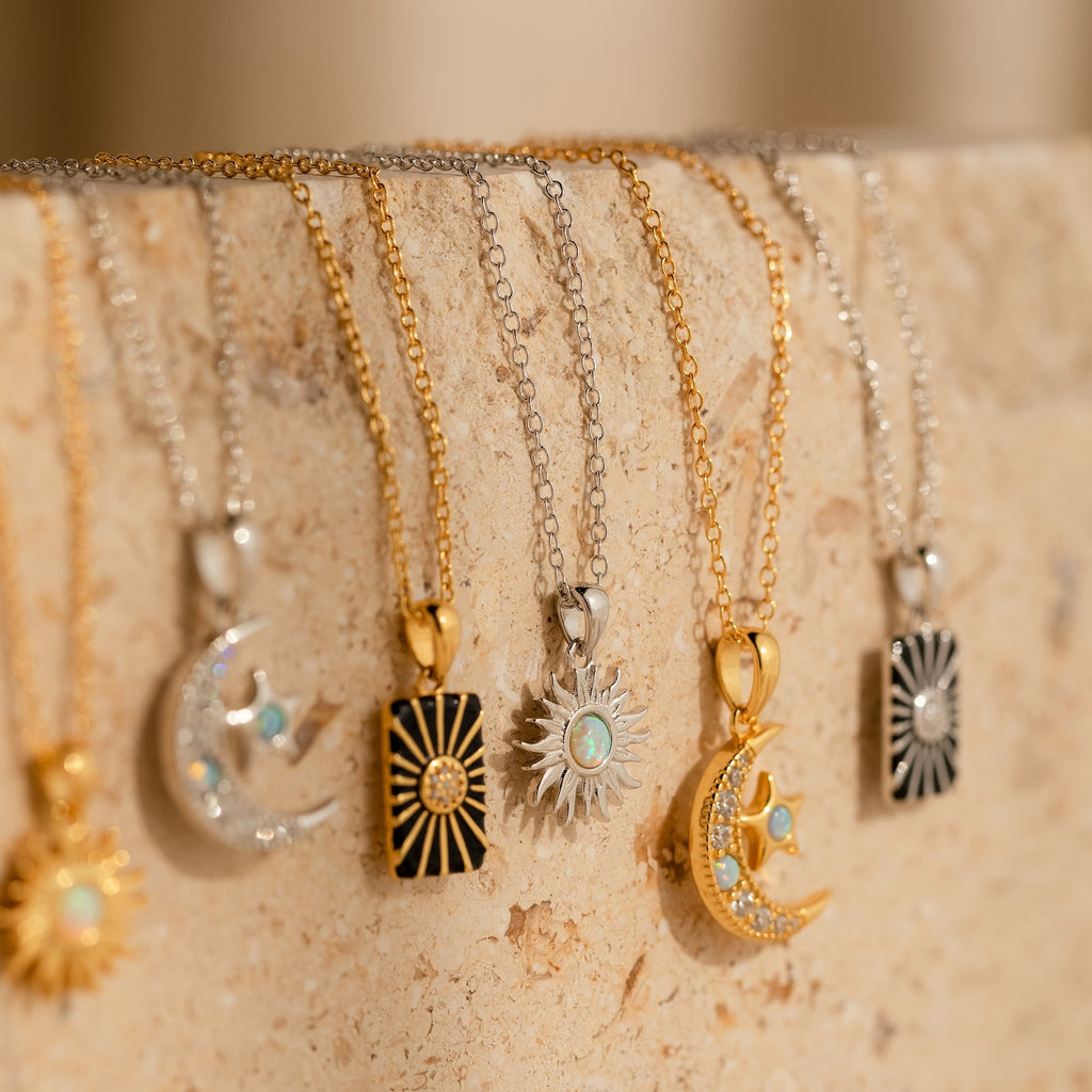 Five gold and silver Celestial Pendant Necklace Sets with opal and diamond accents hang gracefully on a beige stone surface—an elegant gift for her.