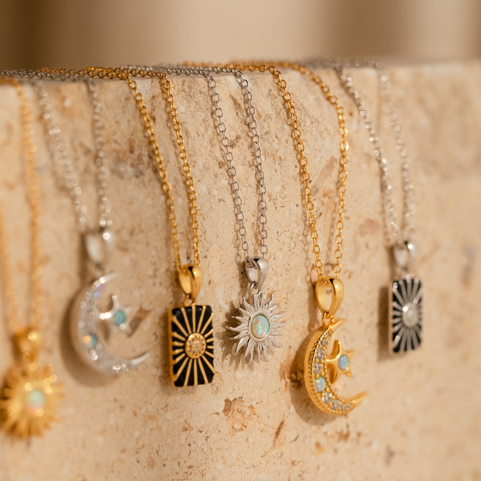 Five gold and silver Celestial Pendant Necklace Sets with opal and diamond accents hang gracefully on a beige stone surface—an elegant gift for her.